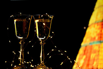 Two glasses with champagne and a decorative Christmas tree in lights on a black background.