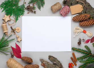 Christmas holiday background with Natural wooden decorations, empty white paper, pine cones and branches on gray.