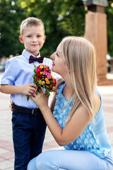 a charming 6-year-old blond boy in a light shirt and bow tie with a small bouquet of flowers with his mother, a beautiful blonde 30 years old in a blue pantsuit