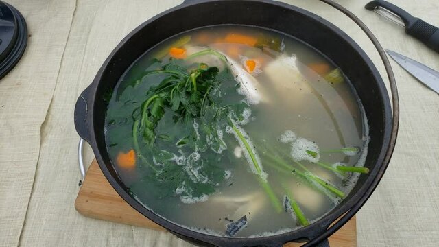 Fish soup freshly made in cast iron pot over fire pit while at camp site.