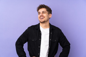 Caucasian man isolated on purple background posing with arms at hip and smiling