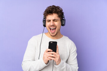 Caucasian man isolated on purple background listening music with a mobile and singing