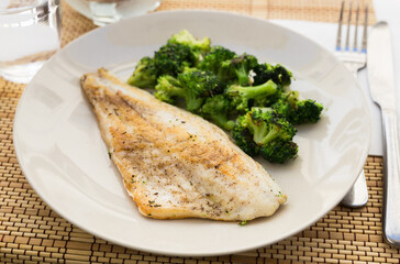 fried fillet of sea bass with garnish of broccoli on black warm stone plate