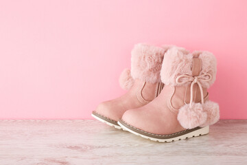 Leather warm kid boots with fluffy balls on wooden floor at light pink wall. Pastel color. Closeup....