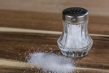 Auf einem hölzernen Brettchen steht ein Salzstreuer, davor auch etwas Salz