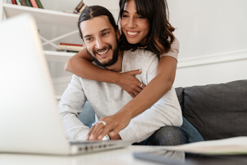 Image of cute cheerful couple using laptop and hugging