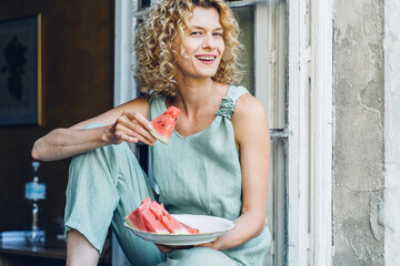 Funny brunette woman get ready with appetite bites of watermelon in cozy kitchen interior...