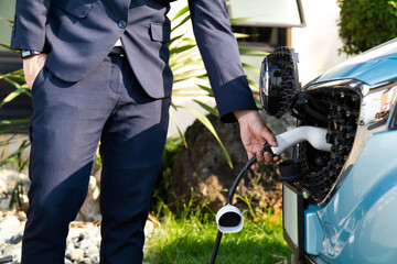 Business man in suite while charging electric car. Power supply for electric car charging. Electric...