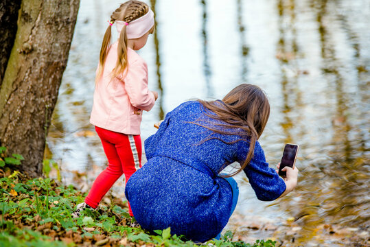 Mother and daughter take pictures of ducks in autumn Park
