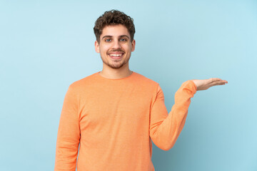 Caucasian man isolated on blue background holding copyspace imaginary on the palm to insert an ad