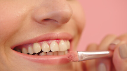 Naklejka premium Young caucasian woman applying lip shine using professional make up brush. Close up. High quality photo
