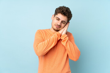 Caucasian man isolated on blue background making sleep gesture in dorable expression