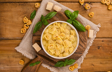 Tortellini mignon on a wooden board with basil and parmesan. Specialties of the cuisine from Bologna and Emilia Romagna: Cappelletti, fresh egg pasta with meat and vegetables filling. Copy space