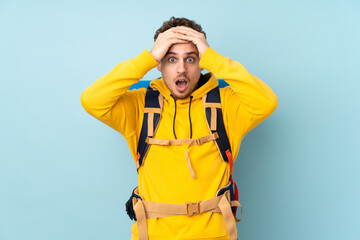 Young mountaineer man with a big backpack isolated on blue  background with surprise facial expression