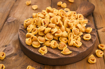 Tortellini mignon on a wooden board and parmesan. Specialties of the cuisine from Bologna and Emilia Romagna: Cappelletti, fresh egg pasta with meat and vegetables filling. Copy space