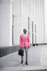 Men's Fashion. A stylish young man dressed in business style in a pink jacket poses on the street of a high-rise building. 