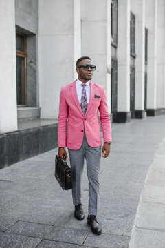 Men's Fashion. A stylish young man dressed in business style in a pink jacket poses on the street of a high-rise building. 