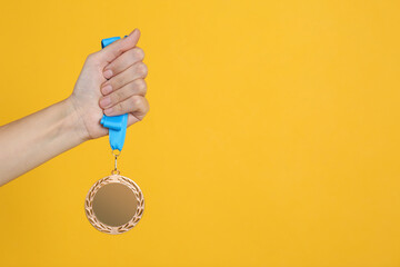 Woman holding bronze medal on yellow background, closeup. Space for design