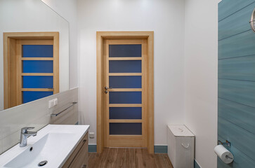 Fototapeta na wymiar Contemporary interior of bathroom in apartment. View of wooden door. Sink and mirror.