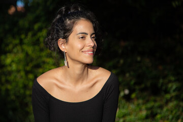 A model woman at a photo shoot. She wears curly hair, bijouterie earrings and a black dress in the late afternoon. Brazilian model. Lifestyle. Fashion. Golden hour.