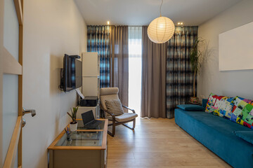 Contemporary interior of living room in modern flat. Cozy couch and chair. Window with curtains. Laptop and printer.