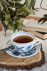 themed coffee corner with dried eucaliptus and bay leaves and retro tablecloth, autumn vibes, bohemian porcelain ornamental mug on the wooden cut with the bark, books in the background