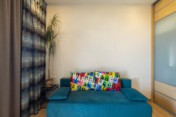 Contemporary interior of living room in modern apartment. Cozy blue couch with pillows. Green palm.