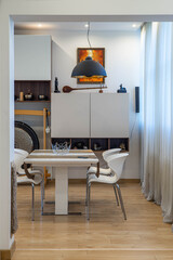 Contemporary interior of living room in luxury flat. Chairs and table. Stylish white wall unit with decorations.