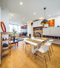 Modern interior of living room in luxury flat. Table and chairs. Home decor. Tibetan bowls and decorative gong. White wall unit with TV.