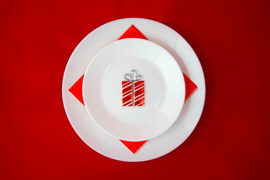 Festive table setting for Christmas and New Year  with empty  white plates  decorated with  red napkin and small present  on red background. Holiday Decorations. Top view.