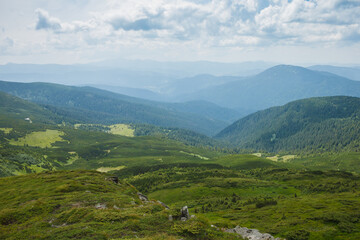 Mountain landscape. A view of the mountains with green meadows and coniferous forests against the background of beautiful clouds 