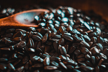 Fried sunflower black seeds with a wooden spoon in a pan, close-up