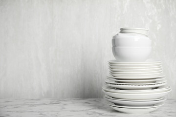 Stack of clean tableware on white marble table. Space for text