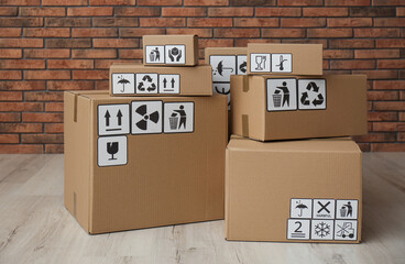 Cardboard boxes with different packaging symbols on floor near brick wall. Parcel delivery