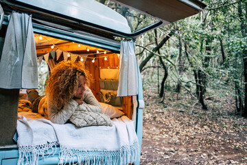 Happy free beautiful woman lay down and relax inside her blue van vehicle parked in the forest -...