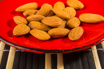 Almonds nuts in a red saucer on a bamboo mat, closeup