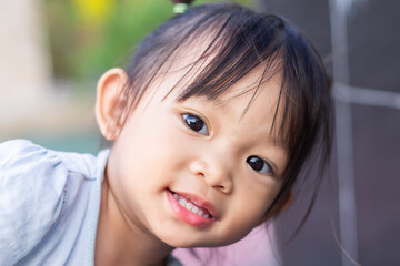 Soft​ focus.​ Portrait image of 1-2 years old baby. Happy Asian child girl smiling and relaxing at the garden park. Pretty girl wearing a white shirt. Summer season. Kids and healthy concept.
