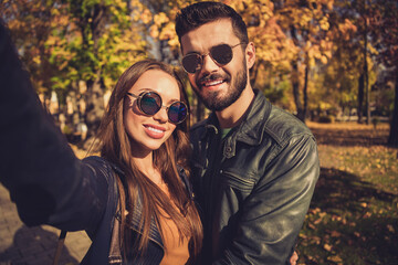 Portrait of positive romantic dream couple make selfie in fall september forest town park wear glasses jacket