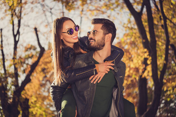 Photo of positive couple guy hug piggyback beloved girlfriend in september orange town park wear jacket sunglass