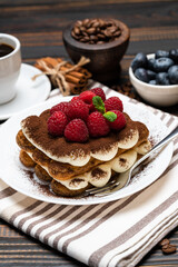 portion of Classic tiramisu dessert with raspberries. blueberries and cup of espresso coffee isolated on wooden background