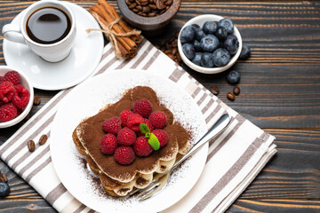 portion of Classic tiramisu dessert with raspberries. blueberries and cup of espresso coffee isolated on wooden background