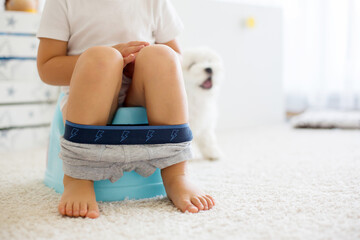 Blond toddler child, using potty at home, little pet maltese dog next to him