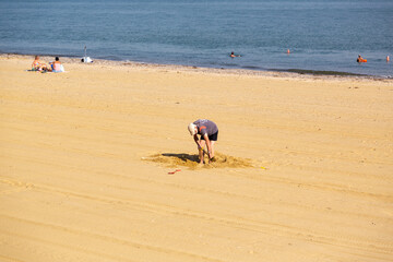 A middle aged man digging in the sand on a beach with a bucket and spade