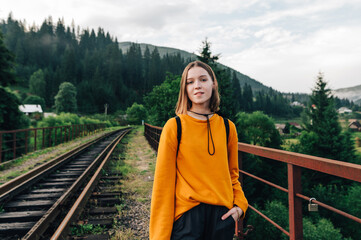 Portrait of a positive hipster woman in casual clothes walking on the track of a railway mountain...
