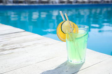Refreshing cocktail near outdoor swimming pool on sunny day. Space for text