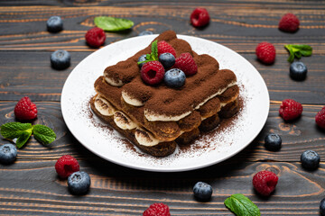 portion of Classic tiramisu dessert with raspberries and blueberries on wooden background