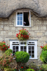 A close up of an exterior of an old thatched cottage with hanging baskets and flowers in front