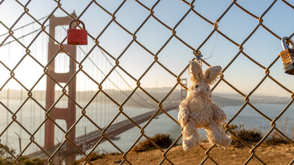Toy bunny rabbit locked to a wire fence overlooking the Golden Gate Bridge