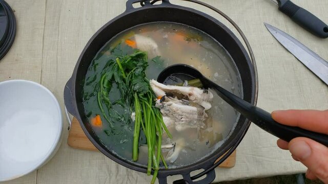 High angle view of cast iron pot of hot fish soup being checked with ladle.