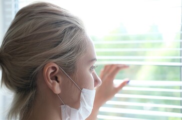 A young woman in a medical mask stands by the window.Prevention COVID-19